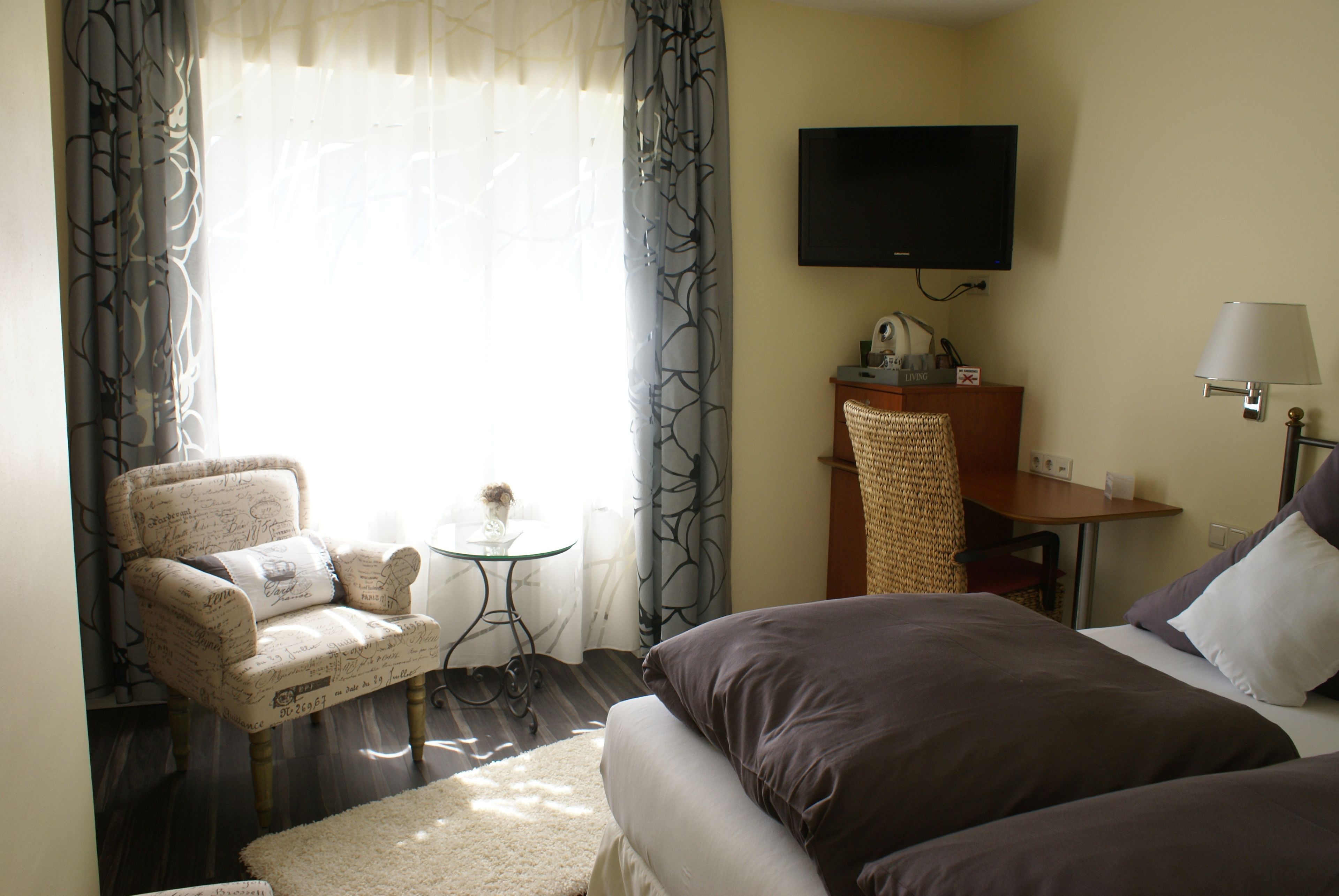 A hotel room with a bed, a chair, a small table, a TV, and a lamp.