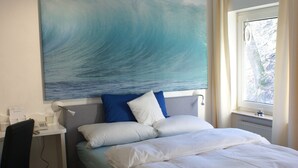 A bedroom with a bed, a desk, and a large painting of a wave.