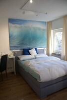 Quarto com uma cama, uma escrivaninha e uma grande pintura de uma onda.