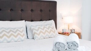 A neatly made bed with two pillows, a bedside table with a lamp, and a stack of towels. - A (VA022) TH Casa Port Saplaya (Alboraya)
