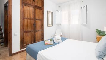 Un dormitorio con cama, un armario de madera, una mesita de noche con lámpara y una ventana con cortinas.