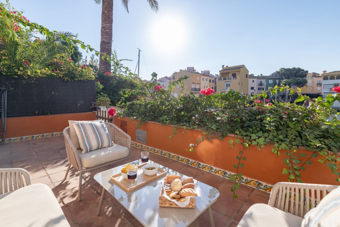 A terrace with wicker furniture, a table with food and drinks, and a view of buildings in the background.