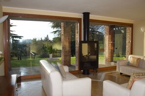 A living room with a fireplace, white sofas, and large glass doors leading to a garden.