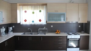 A modern kitchen with dark cabinets, a white countertop, a stainless steel sink, a dish rack, a stove, and a window with decorative stickers. - Bellissima Campagna Home<br>Pelekapina Chania Crete  (Chania , Crete)