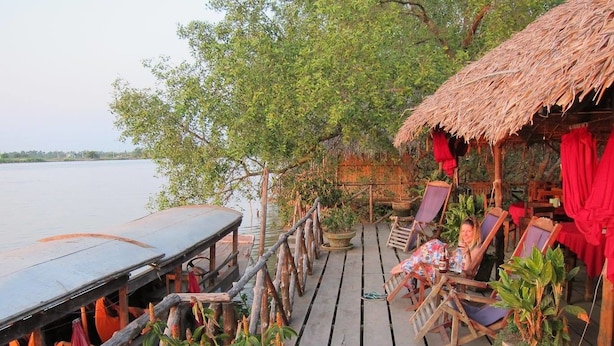 A wooden deck with a thatched-roof structure, outdoor seating, and potted plants. - Happy Family Guesthouse (An Binh)