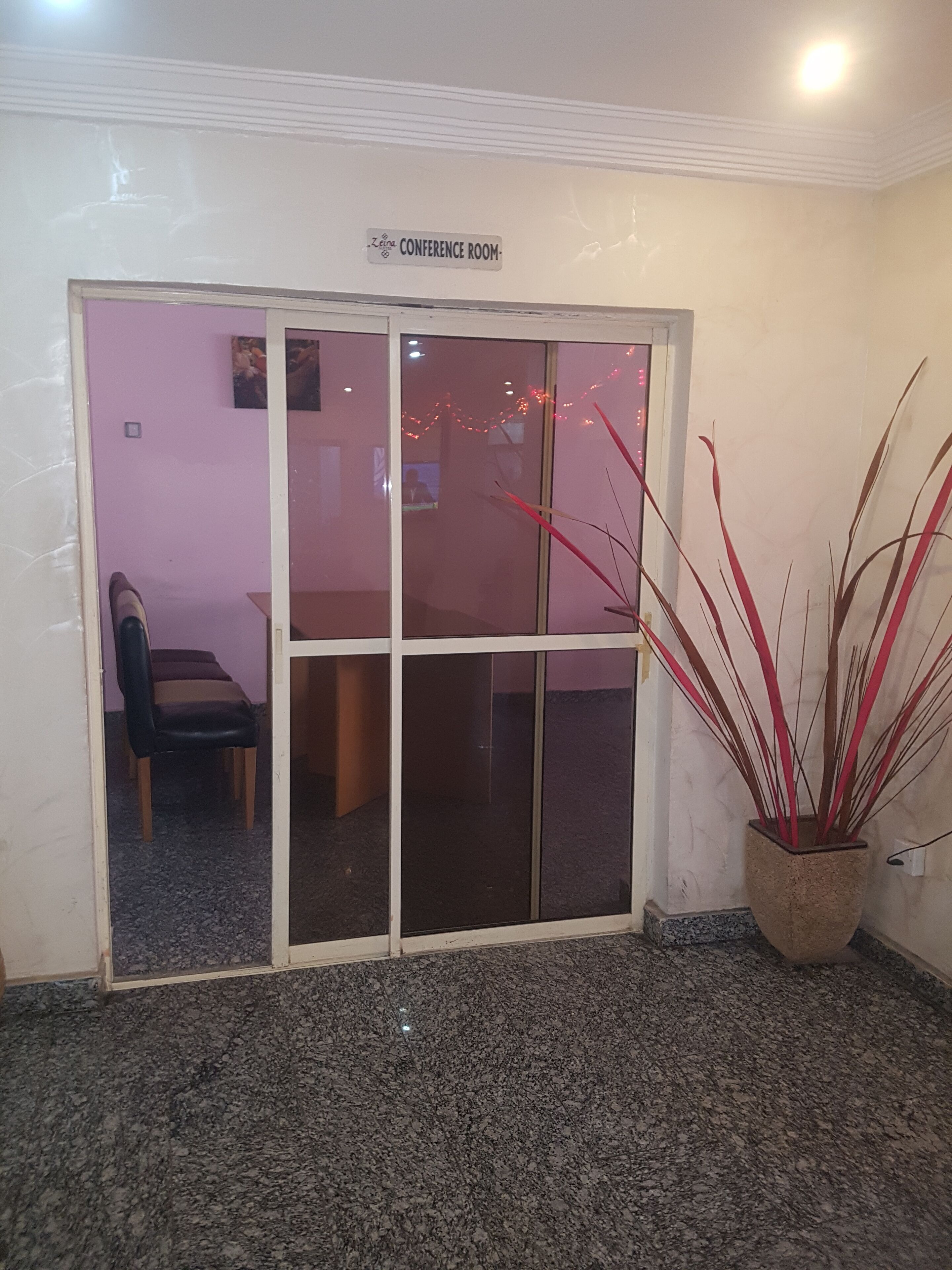 Uma sala de conferências com uma placa sobre a porta, um vaso de planta e uma cadeira ao fundo.