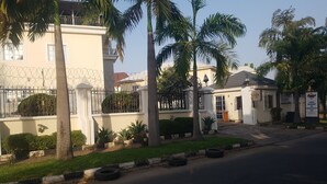 A building with a gated entrance, palm trees, and a sign for a restaurant named "Zina". - Zeina Suites Abuja (Abuja)