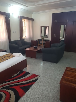 Ein Hotelzimmer mit einem Bett, zwei Sofas, einem Couchtisch, einem Schreibtisch, einem Stuhl, einem Spiegel und einem Kleiderschrank.