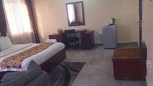 A hotel room with a bed, a desk, a chair, a small refrigerator, and a sofa. - Zeina Suites Abuja (Abuja)