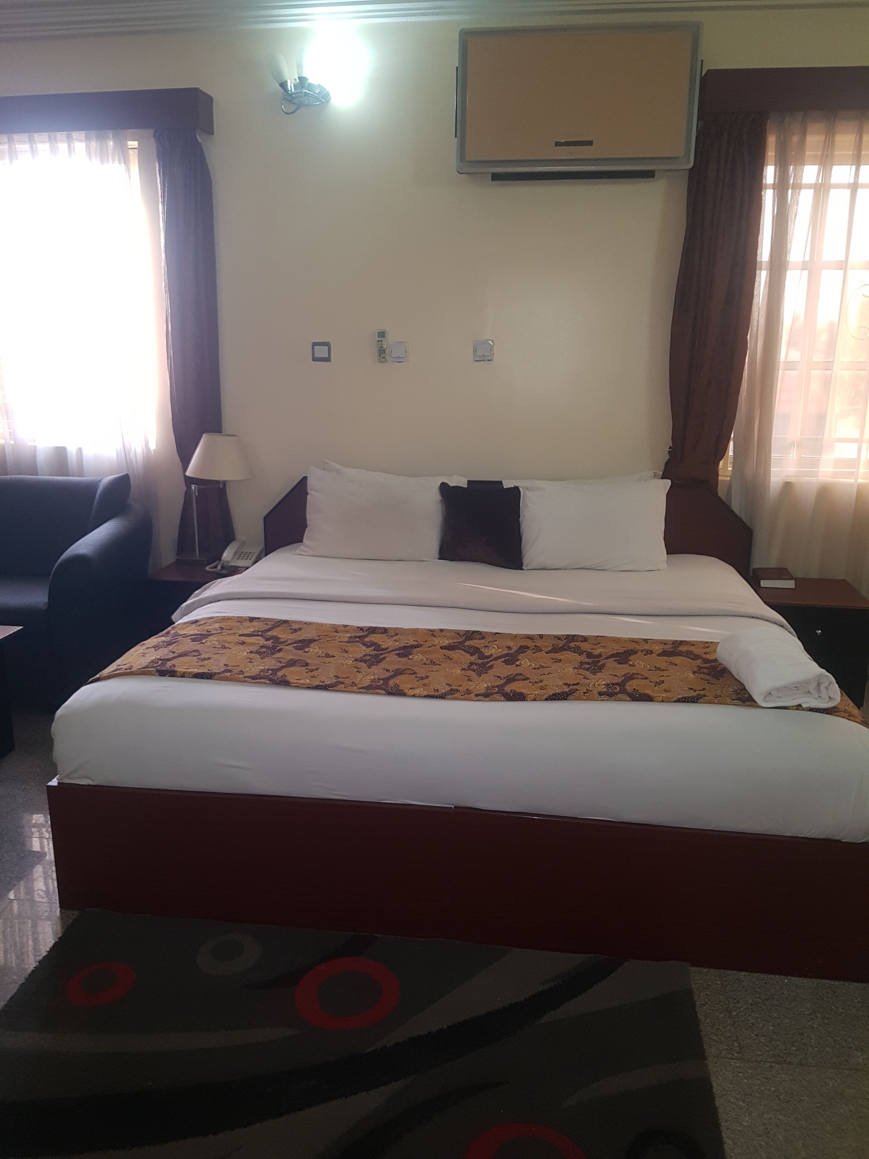 A hotel room with a bed, a desk, a chair, a lamp, and a window with curtains.