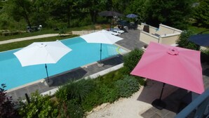 A swimming pool with umbrellas, surrounded by greenery and a view of the countryside.