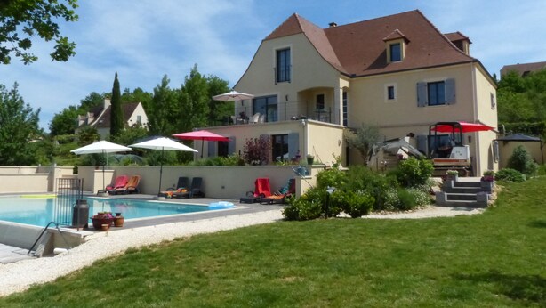A two-story house with a swimming pool, outdoor seating, and a lawn.