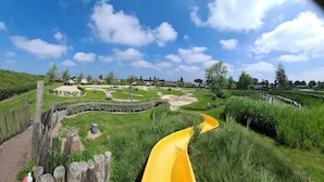 A park with a yellow slide, a wooden fence, and a clear blue sky.