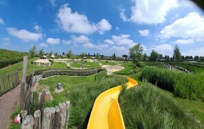 A park with a yellow slide, a wooden fence, and a clear blue sky.