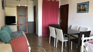 Een kamer met een bed, een televisie, een eettafel met stoelen en een rood gordijn.