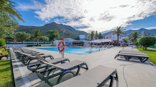 A poolside area with lounge chairs and a lifebuoy, surrounded by greenery and mountains. - Agi Rescator 218 Apartamento for rent in Roses Girona. (Roses)