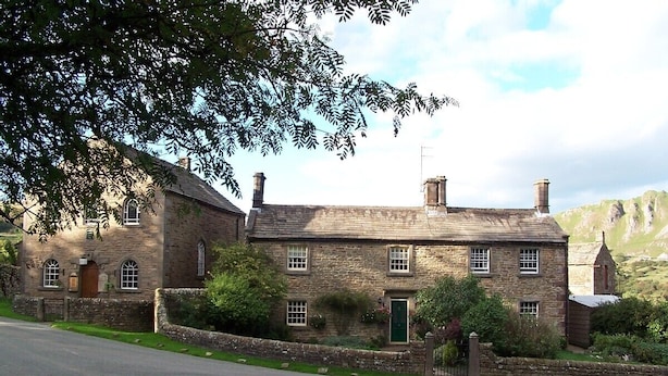 A stone building with a green door, multiple windows, and a chimney.