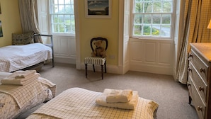 A bedroom with two beds, a chair, a dresser, and large windows.