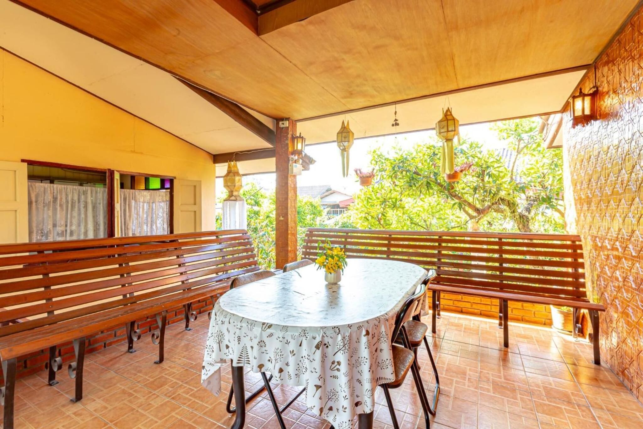 A covered patio area with wooden benches and a round table with a floral tablecloth.