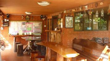 A rustic bar area with wooden stools, a long wooden bench, and a counter with various items.