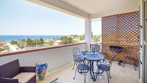 En balkon med et bord, stole, en fletsofá og havudsigt.