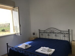 Ein Schlafzimmer mit einem Metallbettgestell, einer blauen Bettdecke und zwei ordentlich gefalteten weißen Handtüchern auf dem Bett.