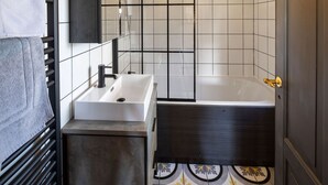 Un baño con un lavamanos blanco, una bañera negra y baldosas de suelo con diseño.
