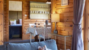 Un interior de cabaña acogedor, con una cama, una mesa de comedor con sillas, un sofá y una lámpara.