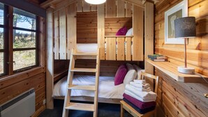Una habitación acogedora de estilo cabaña con una litera, un escritorio con lámpara y ventana con vistas al exterior.