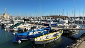 Un port esportiu amb nombroses embarcacions amarrades, cel blau i edificis al fons.