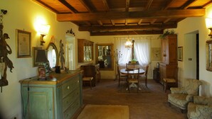 A traditional room with wooden beams, a dining table with chairs, a cabinet, and a chandelier.