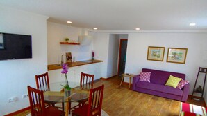 A living room with a purple sofa, a dining table with chairs, a kitchen area, and a TV mounted on the wall. - Relaxing Casa do Atlântico - Funchal (Funchal)