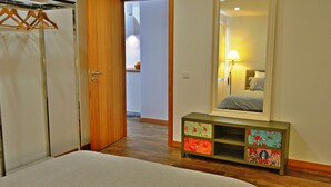 A bedroom with a bed, a wooden wardrobe, a dresser with decorative boxes, and a large mirror reflecting a bed and a lamp. - Relaxing Casa do Atlântico - Funchal (Funchal)