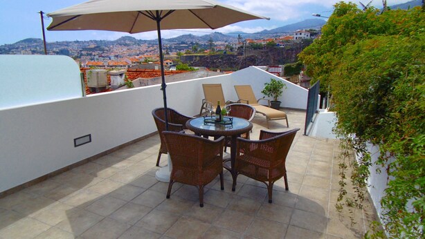 A rooftop terrace with a table and chairs, a large umbrella, and a view of a cityscape. - Relaxing Casa do Atlântico - Funchal (Funchal)