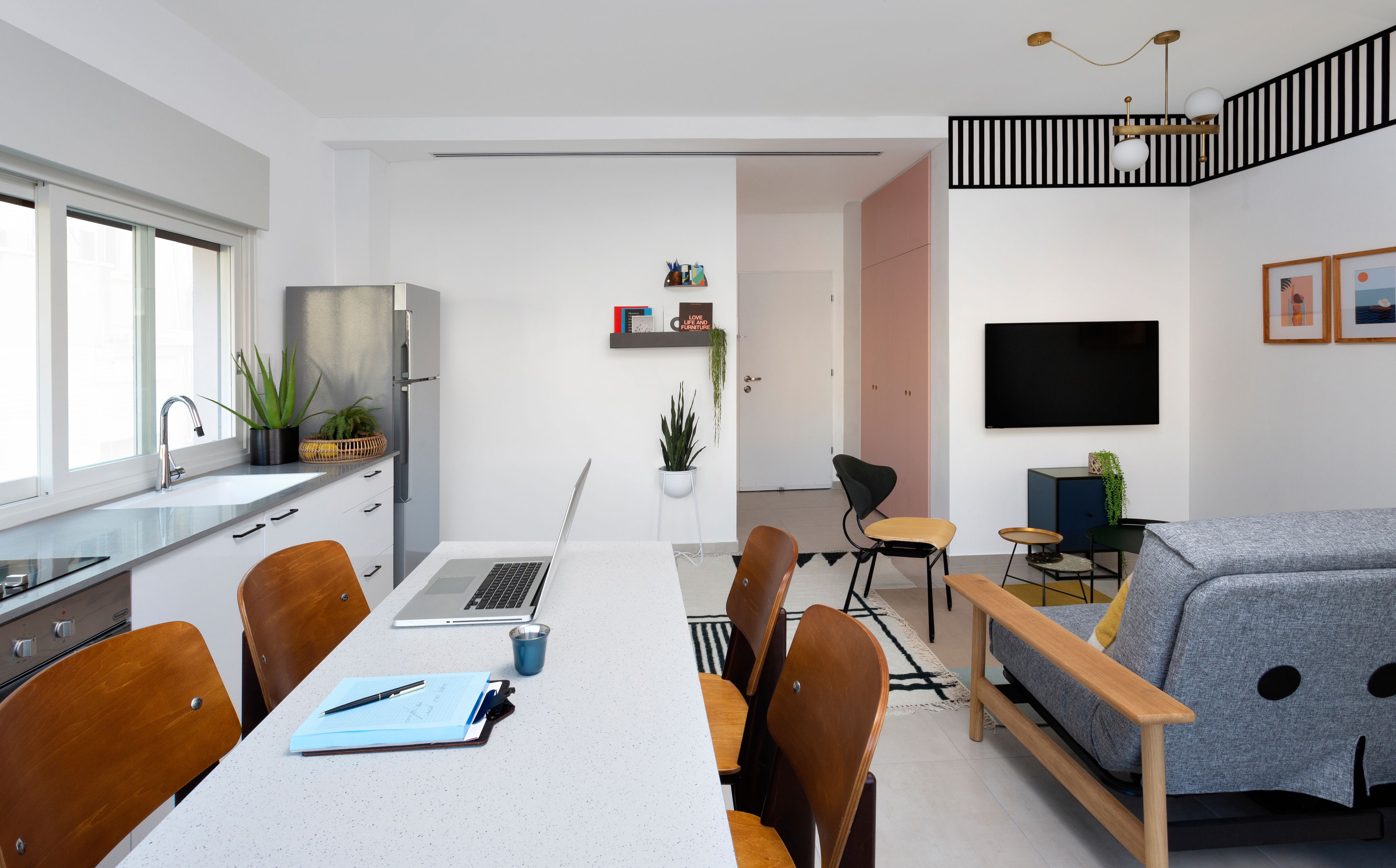 A modern kitchen with a dining area, a sofa, and a TV.