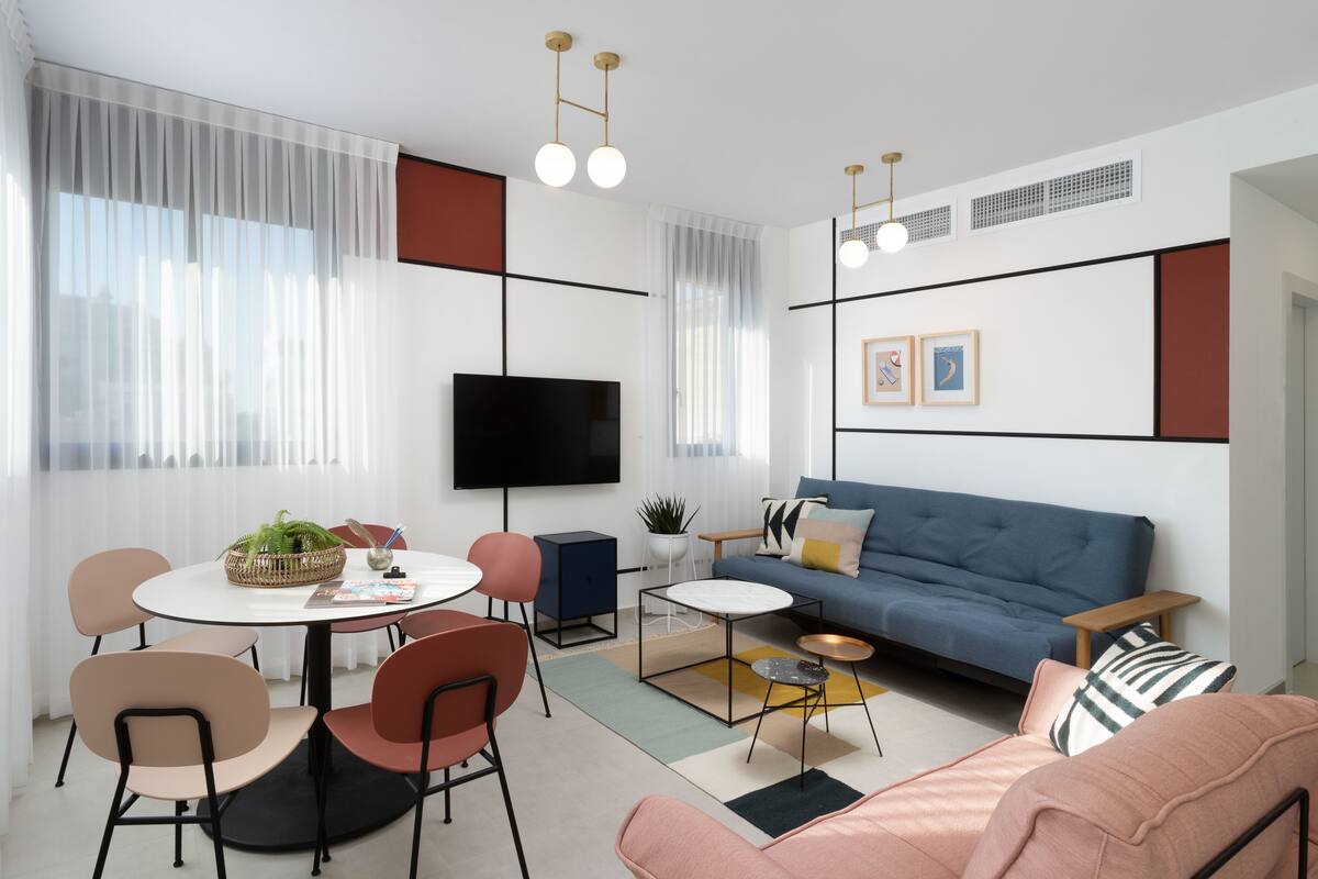 Un salon moderne avec un canapé bleu, une table à manger ronde et des chaises. Un téléviseur à écran plat est fixé au mur, et deux tableaux encadrés sont accrochés au-dessus du canapé.