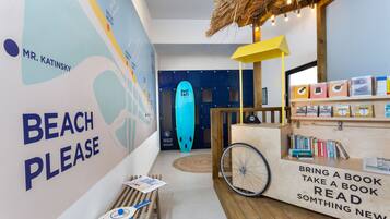 A beach-themed area with a 'BEACH PLEASE' sign, a surfboard, and a bookshelf with books and a bicycle wheel.