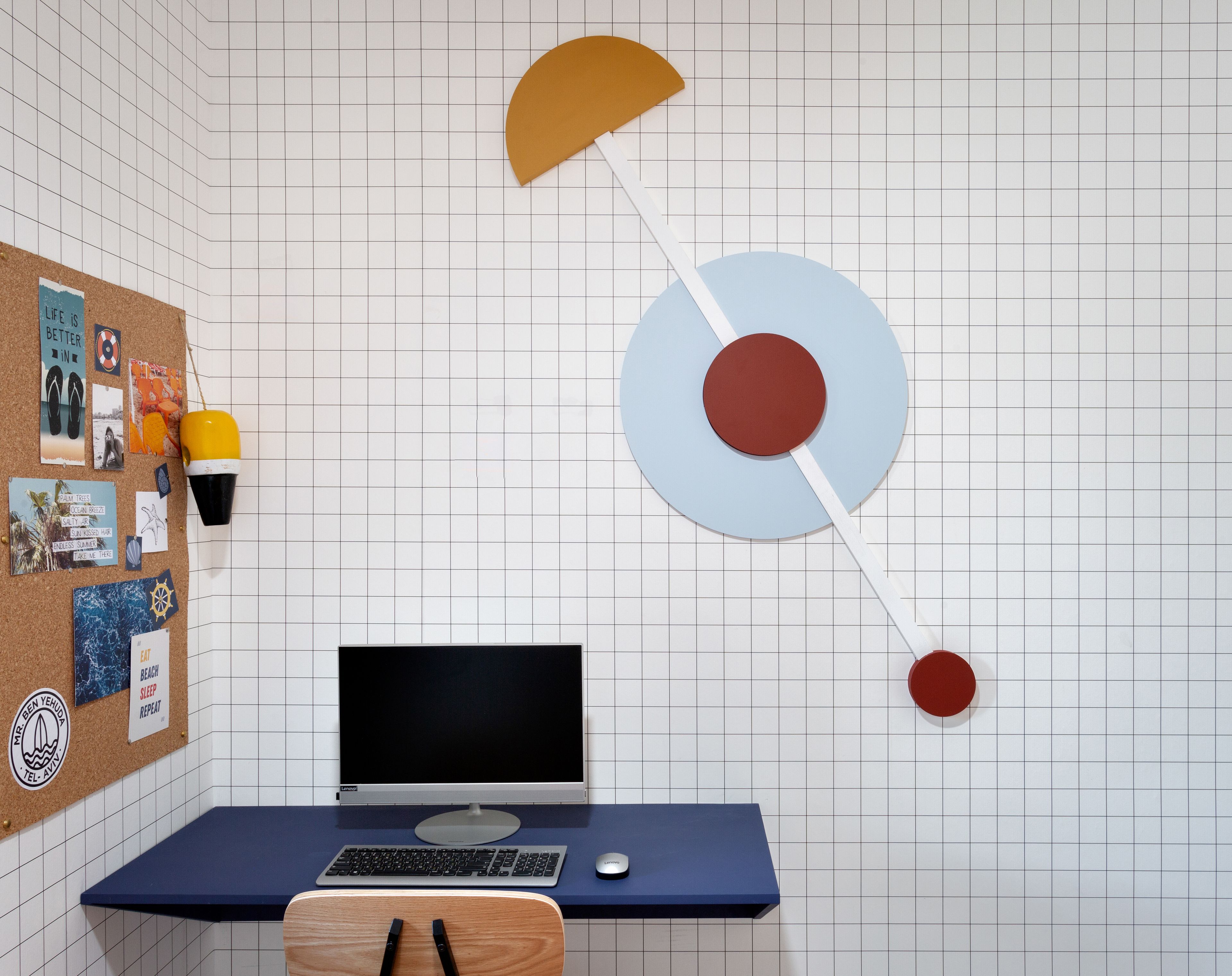 A room with a corkboard filled with photos and notes, a desk with a computer, and a wall-mounted circular decoration.