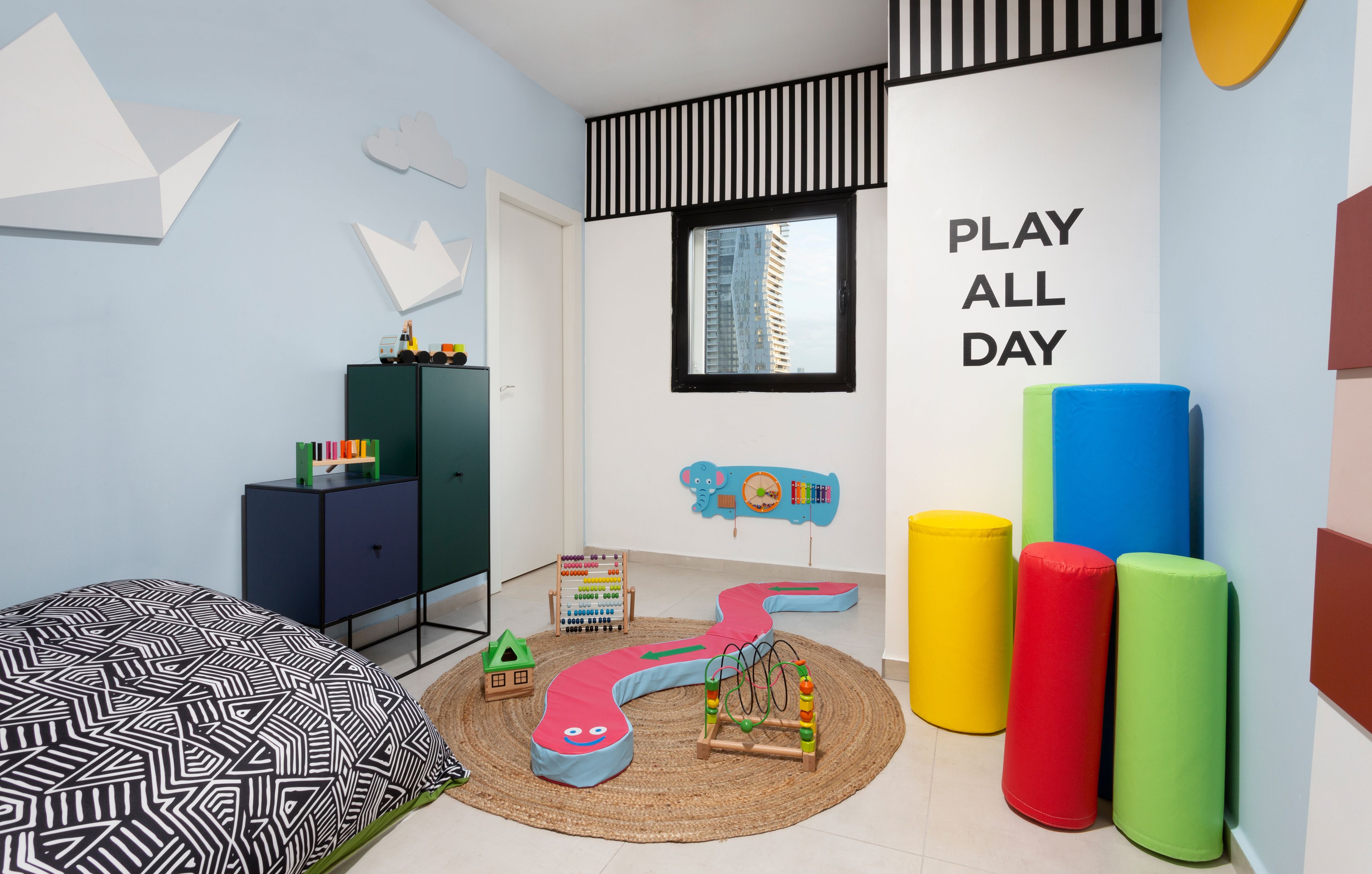 Un cuarto de juegos infantil con un tapete de juegos, juguetes y cojines coloridos.