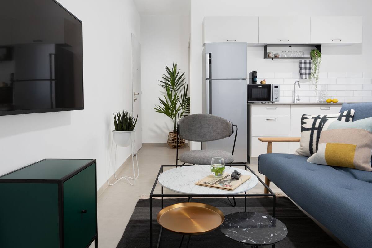 Une cuisine moderne avec des meubles blancs, un four à micro-ondes et un évier. On y trouve également un coin repas avec une table ronde et un canapé bleu.