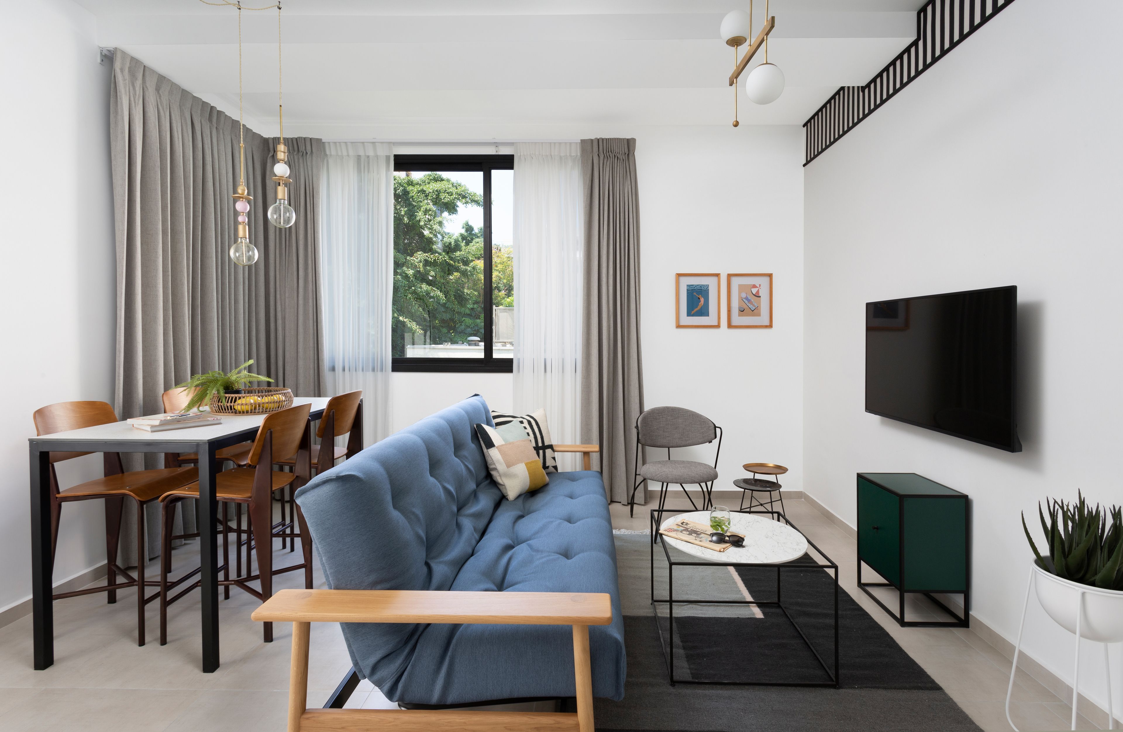 A modern living room with a sofa, dining table, chairs, a TV, and a staircase.