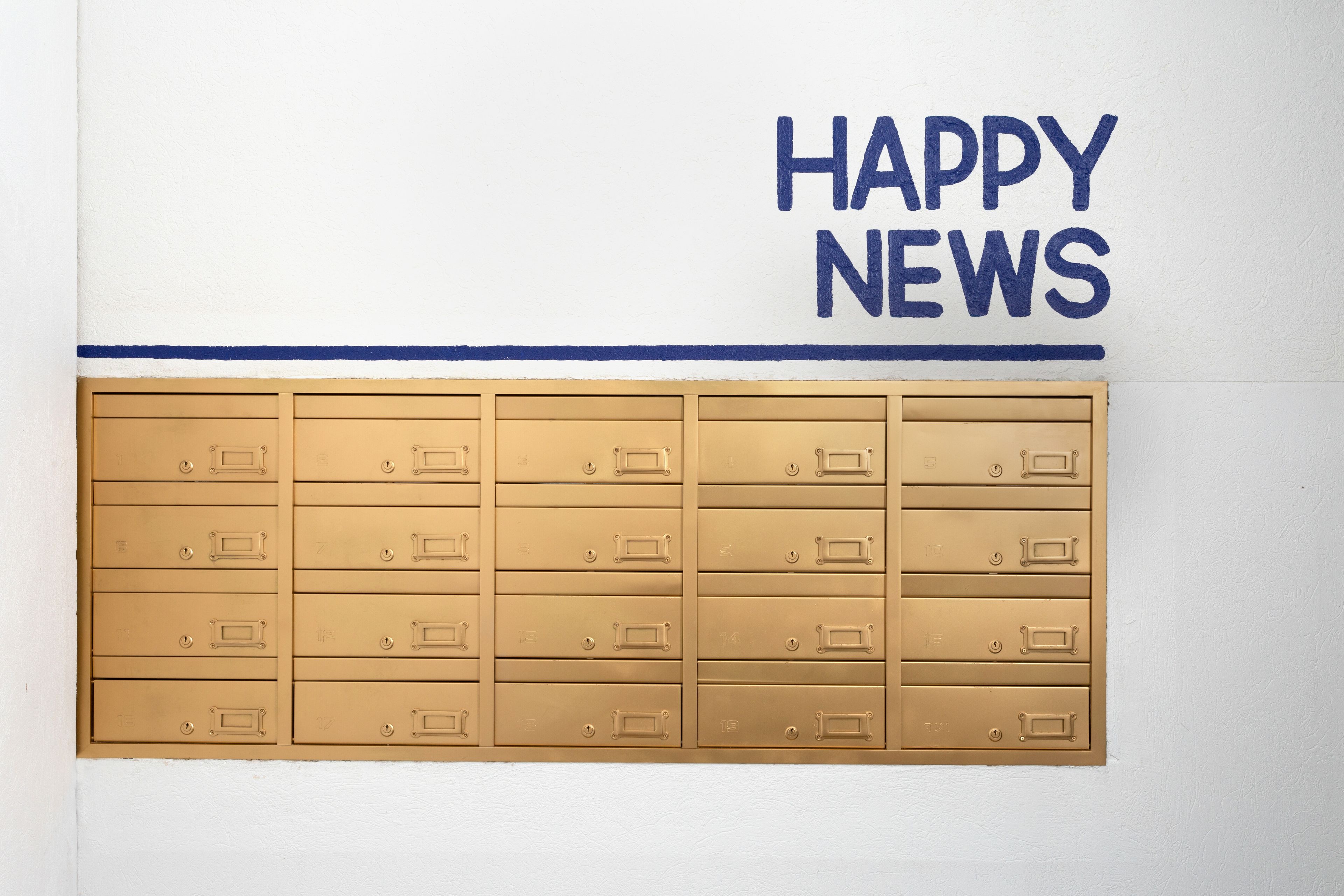Eine Wand mit einer Reihe von Briefkästen und dem Schriftzug 'HAPPY NEWS' darüber.