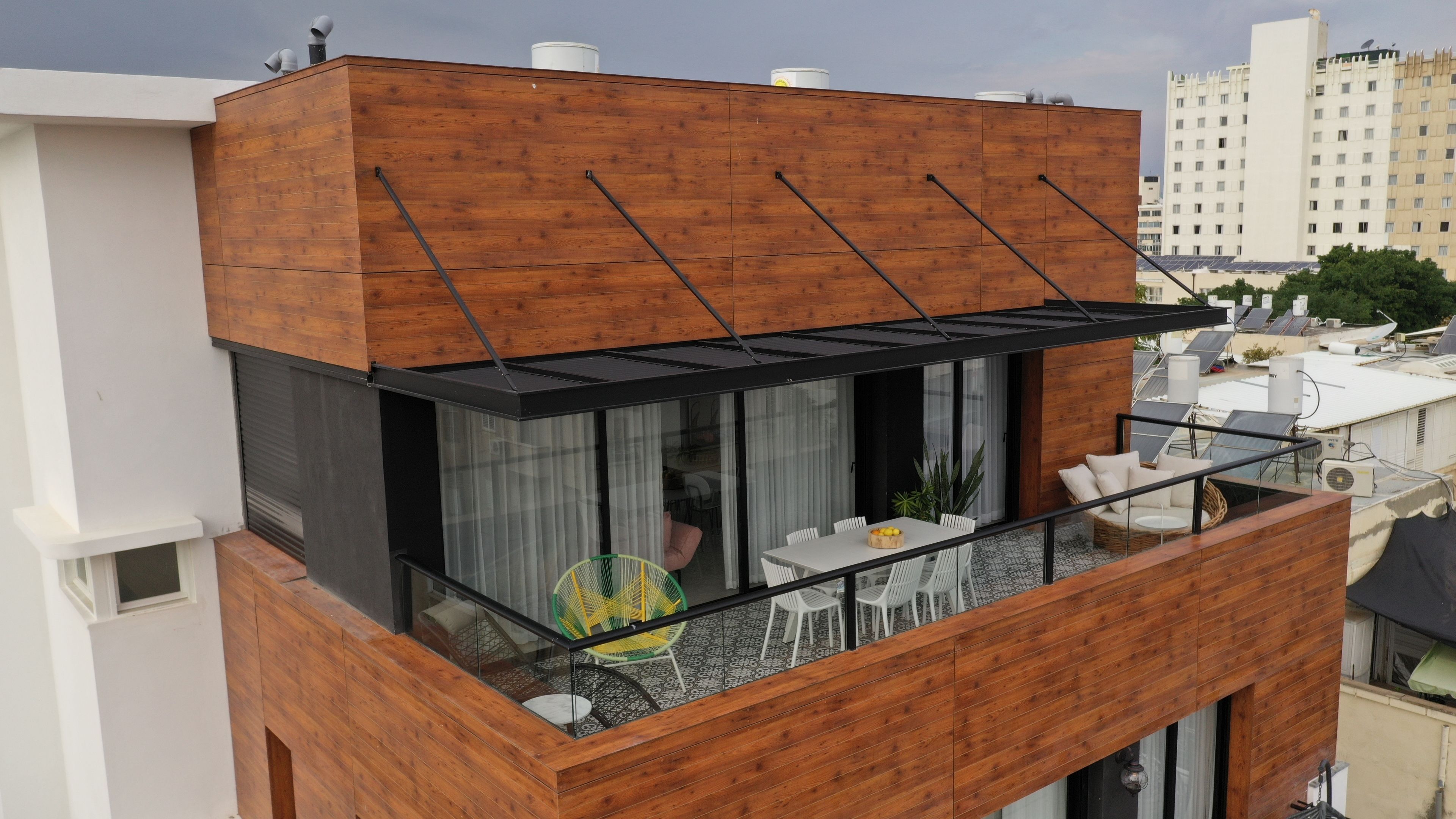 A modern building with a wooden facade, a balcony with outdoor seating, and a view of the cityscape.
