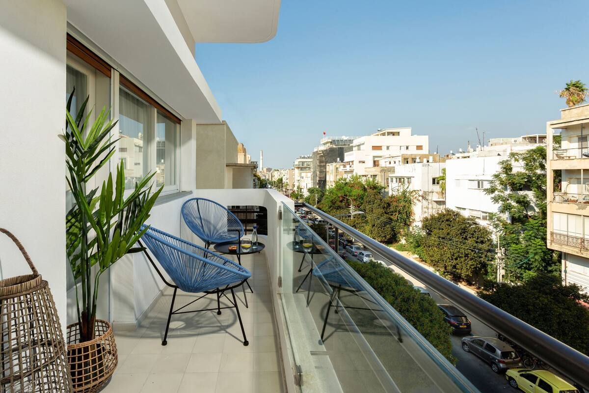 Un balcon avec deux chaises bleues, une petite table et un pot de fleurs.