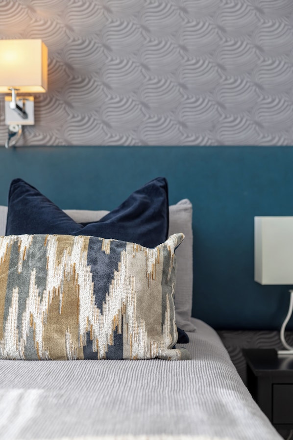 Un lit bien fait, agrémenté d’oreillers à motifs, d’une tête de lit bleue et d’un mur au décor texturé.