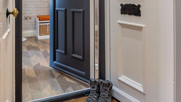 Un pasillo con una puerta azul oscuro, una puerta blanca con una placa de identificación y un par de zapatos en el suelo.