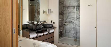 Une salle de bain moderne dotée d’une grande baignoire, d’une douche à parois de verre et d’un meuble-lavabo avec plusieurs vasques et des rangements.