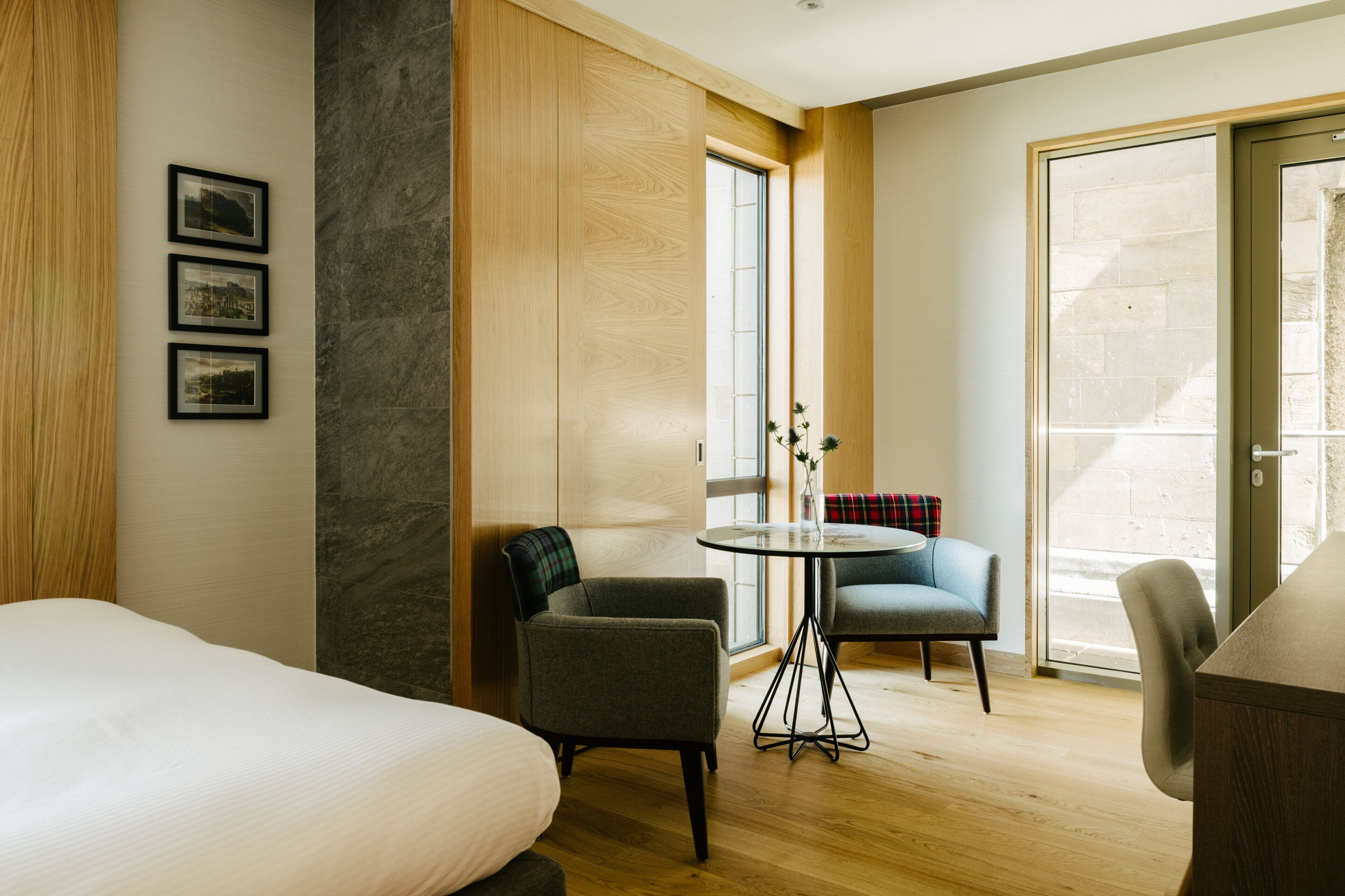 A hotel room with a bed, two armchairs, a small table, and a large window.