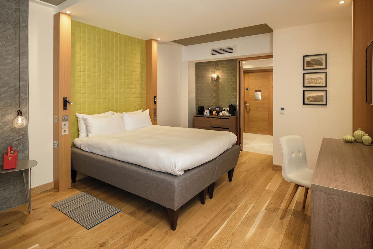 A hotel room with a bed, a desk, a chair, a small table, and a door.