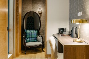 A modern bathroom with a wooden vanity, a chair with a plaid cushion, and a wall-mounted light fixture.